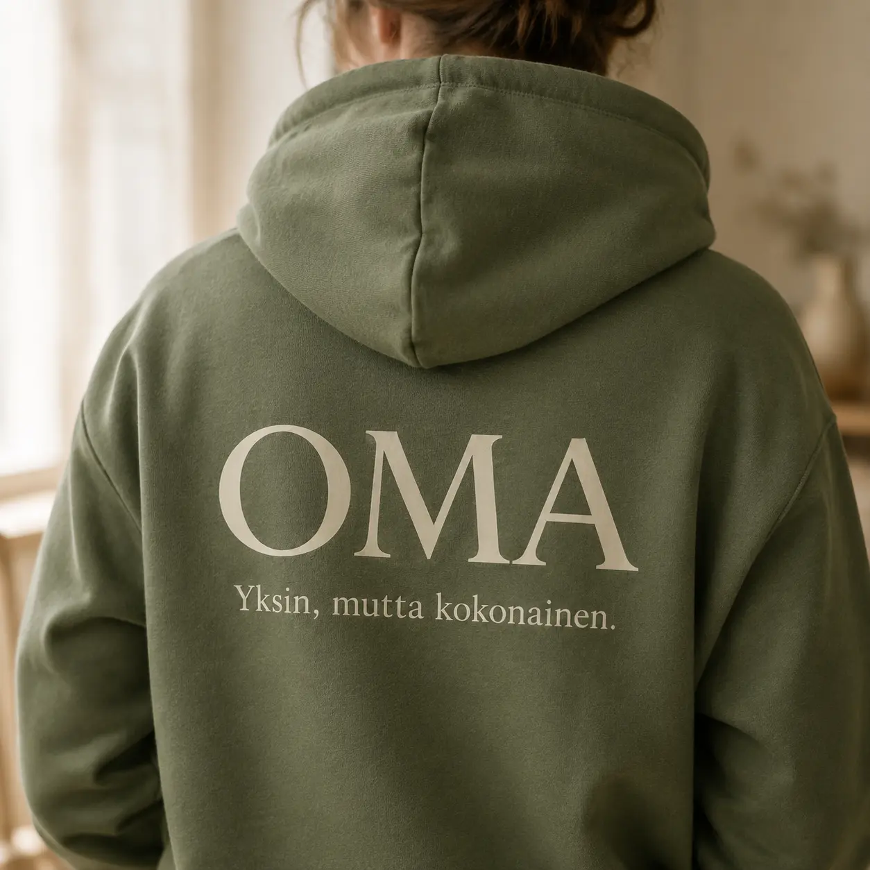 Vihreän OMA-hupparin selkäpuoli, jossa lukee OMA – Yksin, mutta kokonainen.